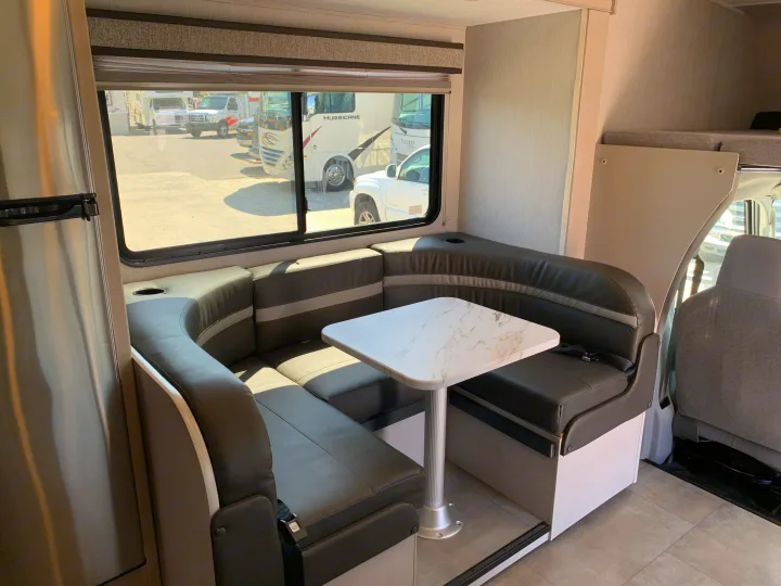 Modern RV rental interior with a spacious U-shaped dinette, marble-top table, and stainless steel fridge.. Coachmen Freelander 2023