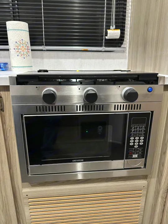 RV rental kitchen: compact stainless steel stovetop and Greystone convection microwave oven with control panel.. Forest River Salem Cruise Lite 2024