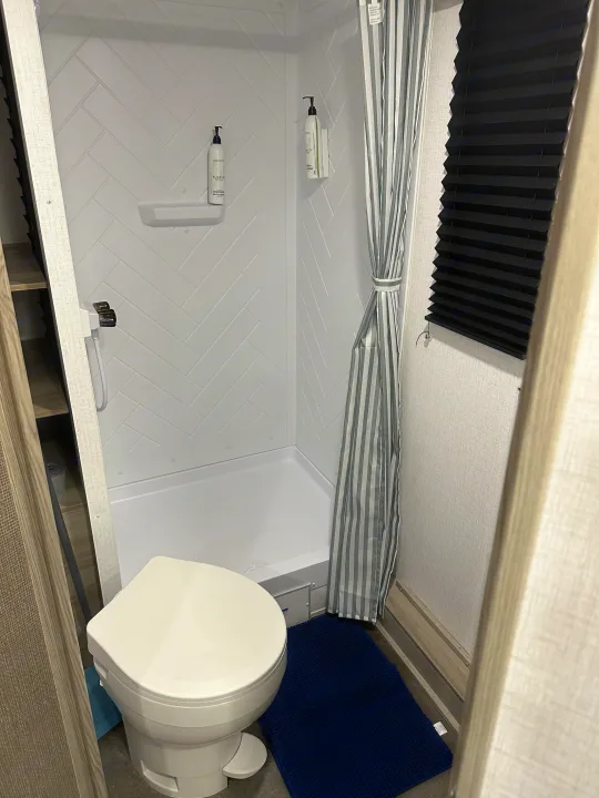 RV rental bathroom: compact shower with herringbone walls, shampoo/conditioner dispensers, toilet, and blue bath mat.. Forest River Salem Cruise Lite 2024