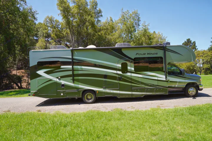 This green Class C motorhome RV rental sits on pavement surrounded by lush greenery, ready for your travels.. Thor Four Winds 2020