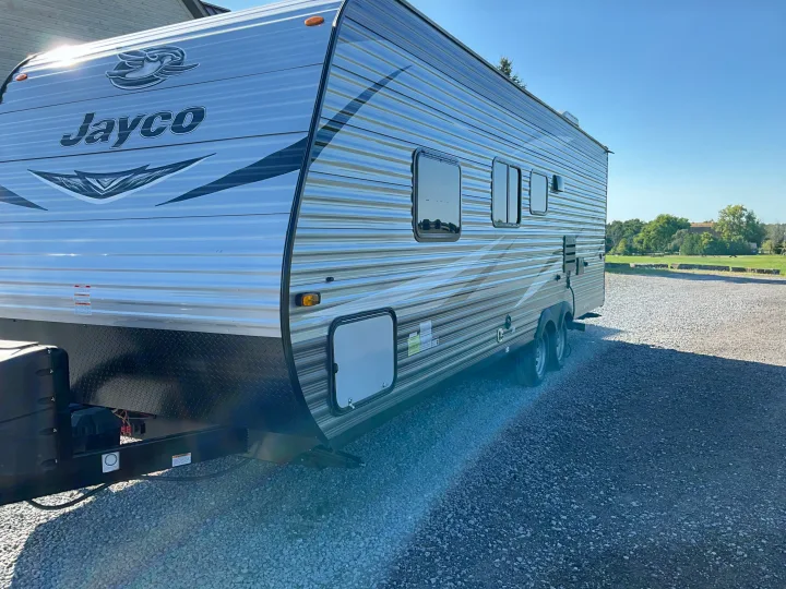 This sleek Jayco travel trailer RV rental, gleaming in the sun on a gravel lot, awaits your next adventure.. Jayco Jay Flight 2021