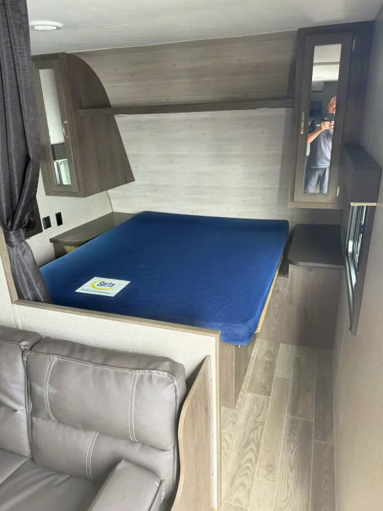 Compact RV rental bedroom featuring a comfy Serta bed, built-in cabinets, and a gray sofa for relaxing.. Jayco Jay Flight 2021