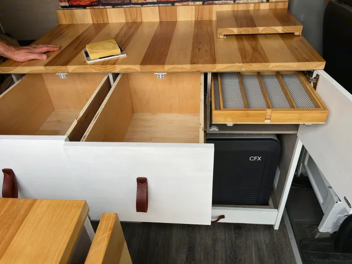 Custom-built RV rental kitchenette with warm wooden countertops, open storage drawers, a cooler, and a clever utensil organizer.. Mercedes Sprinter 2011