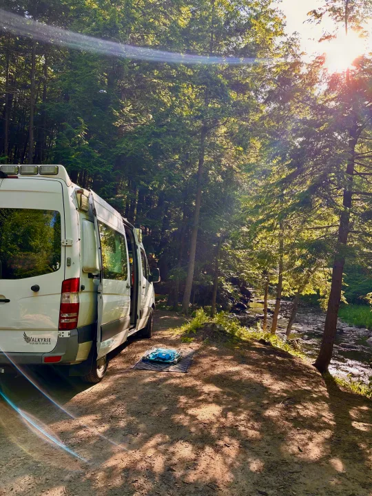 Explore nature with this Valkyrie RV rental, parked by a sun-dappled forest river. Ideal for scenic camping adventures.. Mercedes Sprinter 2011