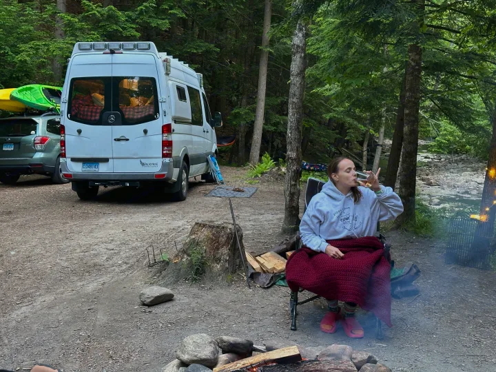 Relaxing by a campfire with an RV rental van and a car carrying kayaks in a lush forest, perfect for outdoor adventure.. Mercedes Sprinter 2011