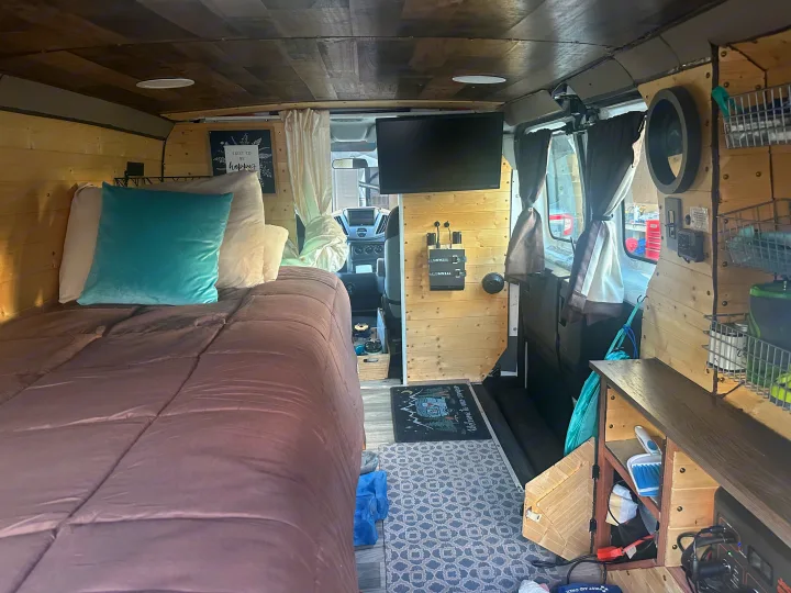 RV rental interior showcasing a comfortable bed, TV, and wooden paneling, offering a cozy travel experience.. FORD TRANSIT 250 2015
