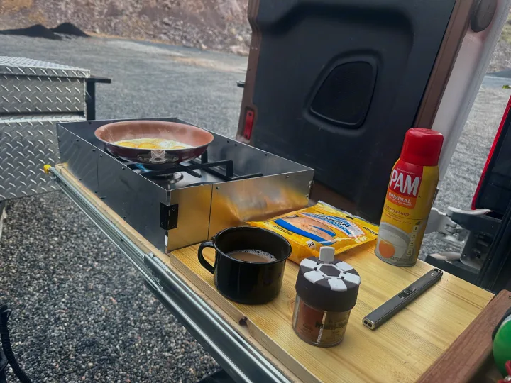 Enjoying outdoor breakfast in an RV rental. Eggs frying on a portable stove with coffee, spices, and cooking spray ready.. FORD TRANSIT 250 2015