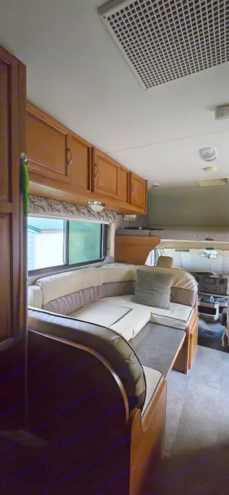 Inside an RV rental: a bright dinette with light cushions, wood cabinets, a large window, and an overhead AC vent.. Winnebago Minnie Winnie 2019