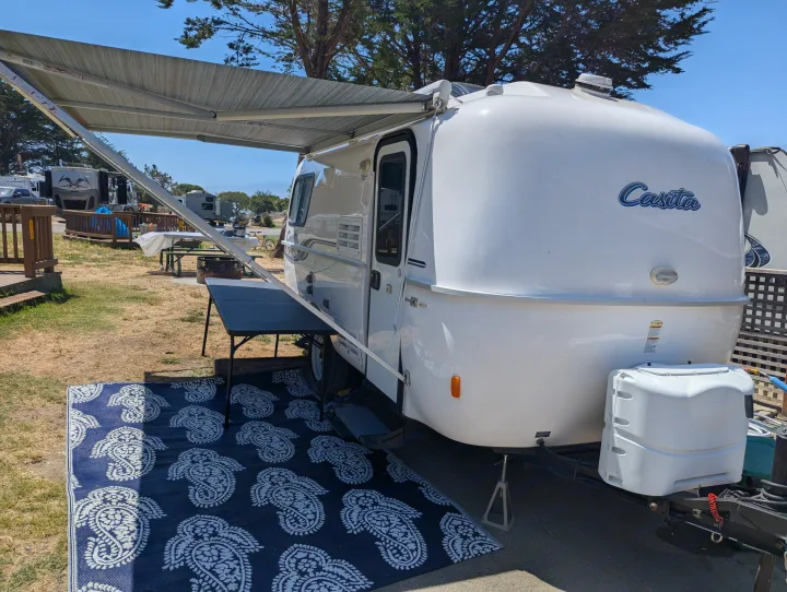 A white Casita travel trailer, perfect for an RV rental, is parked with its awning extended and a patterned outdoor mat.. Casita Casita Trailer 2020