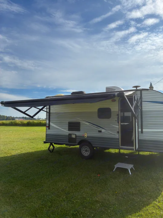 This RV rental is perfectly set up for a peaceful camping getaway, with its awning extended in a green field.. Gulf Stream Ameri-Lite 2019