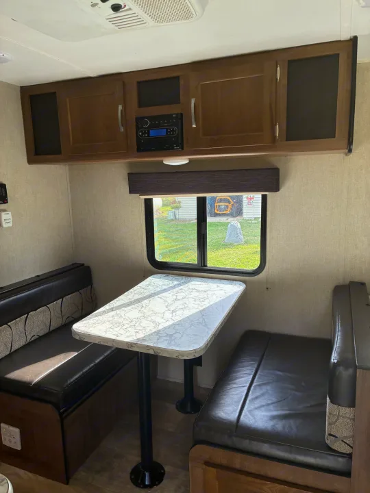 Compact RV rental interior: dinette with marble-look table & leather benches, overhead cabinets, and window view.. Gulf Stream Ameri-Lite 2019
