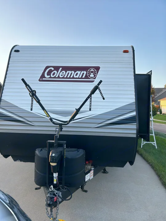 Front view of a Coleman travel trailer with a BikeWing bike rack and propane tanks on the hitch, a type of RV rental.. Dutchmen Coleman Lantern 2020