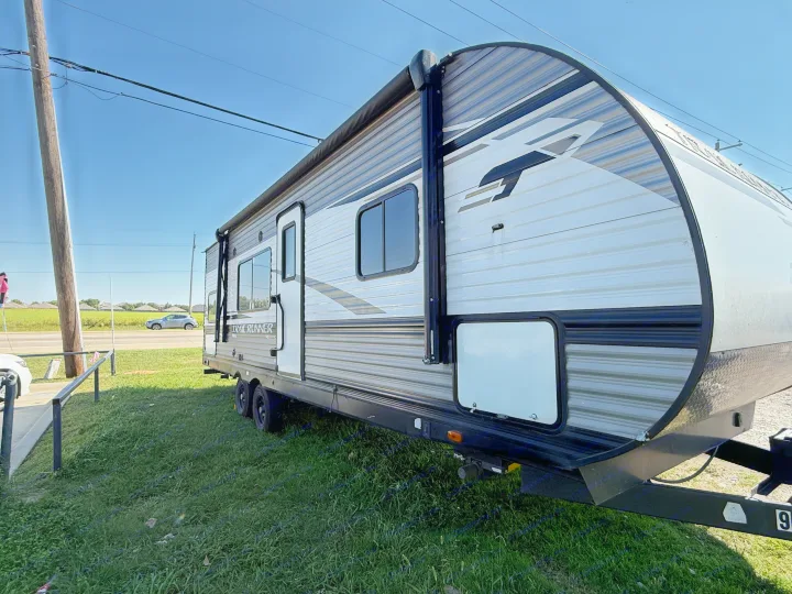 Side view of a grey and white Trail Runner travel trailer, ready for rv rental. Parked on grass on a sunny day.. Heartland Trail Runner 2022
