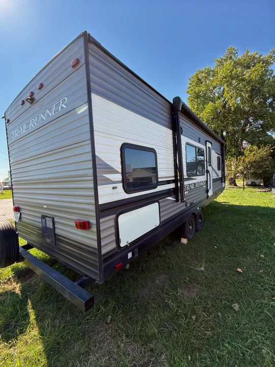 A grey and white Trail Runner travel trailer RV, ideal for an rv rental, parked on green grass under a clear sky.. Heartland Trail Runner 2022