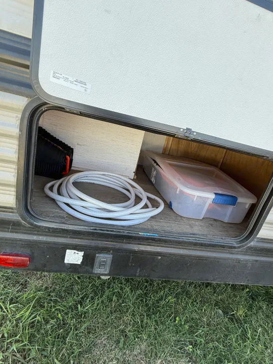 Open RV rental storage: coiled hose, clear bin, and black leveling blocks. Essential gear for your RV adventure.. Heartland Trail Runner 2022