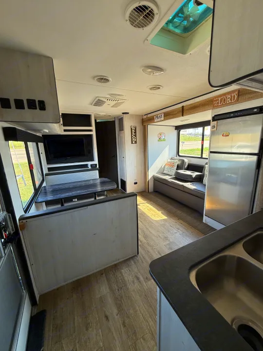 Inside a modern RV rental: well-equipped kitchen, dining booth, sofa, & TV. Comfortable interior for your travels.. Heartland Trail Runner 2022