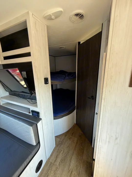 This RV rental interior features cozy bunk beds, a TV in the living space, and light wood grain cabinetry.. Heartland Trail Runner 2022
