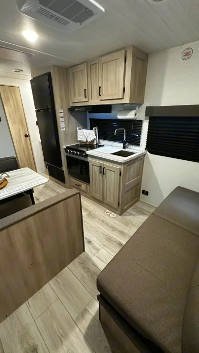 Compact RV rental kitchen with stove, microwave, sink, and fridge. Features a dining table and sofa.. East to West Silver Lake 2024