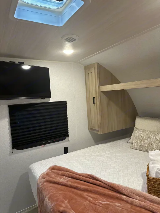 Modern RV rental bedroom with a cozy bed, wall-mounted TV, skylight, and storage. Perfect for comfortable journeys.. East to West Silver Lake 2024