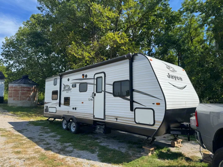 Jayco travel trailer rv rental parked outdoors, stabilized on gravel. Green trees and a rustic silo frame the scene.. Jayco Jay Flight SLX 2016