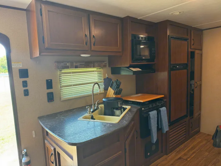 RV rental kitchen featuring wood cabinets, dark counters, a sink, gas stove, microwave, and refrigerator for convenient travel.. Jayco Jay Flight SLX 2016