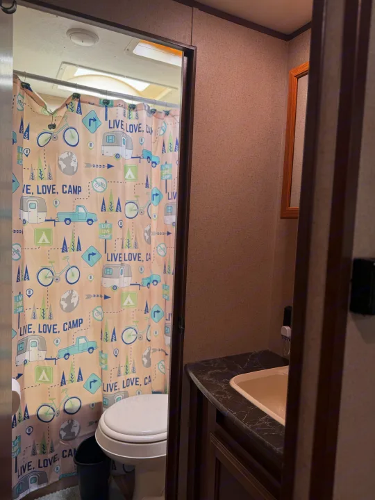 RV rental bathroom with 'Live, Love, Camp' shower curtain, toilet, and sink, designed for compact travel.. Jayco Jay Flight SLX 2016