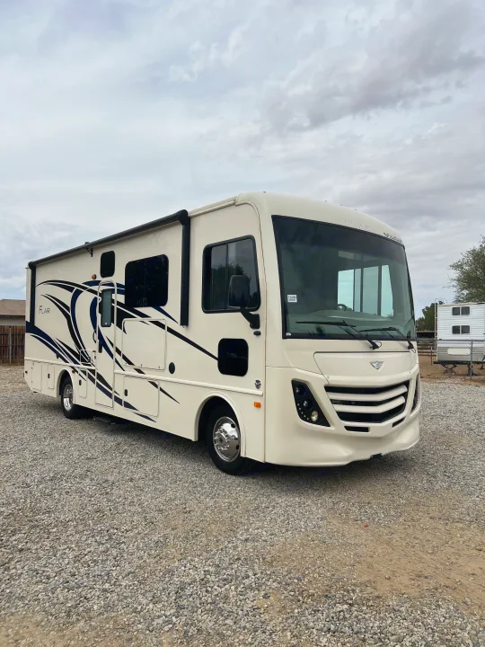 This spacious cream Flair RV rental, featuring striking blue graphics, is parked on gravel, ready for your next adventure.. Flair-Fleetwood Flair-Fleetwood Motorhome 2020