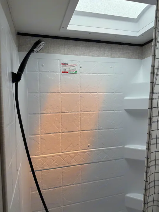 Inside an RV rental: Compact shower with white textured walls, skylight, and handheld showerhead for your adventures.. Jayco Jay Flight SLX 2024