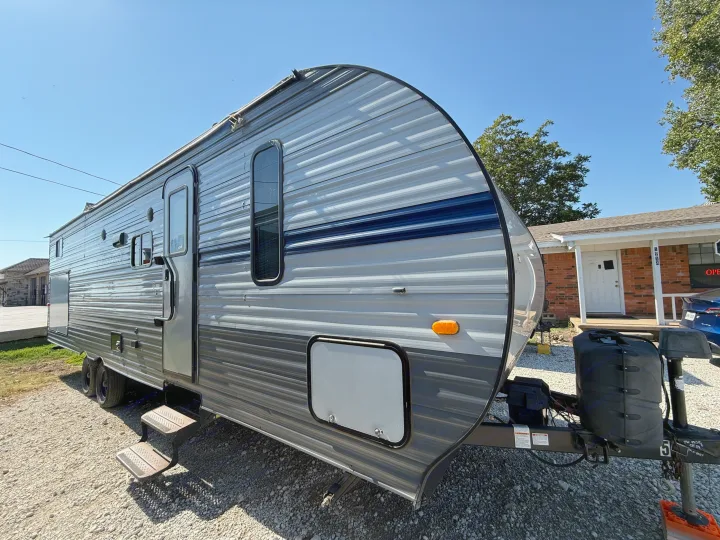 Grey and blue travel trailer RV rental on gravel. Steps extended, ready for camping trips.. Gulf Stream Kingsport 2021