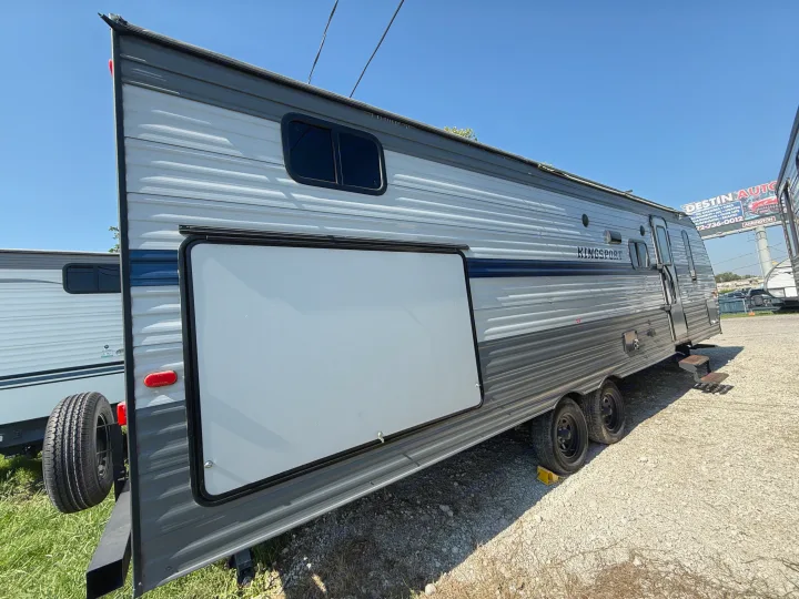 A Kingsport travel trailer for **RV rental**, showcasing its exterior side with a large storage door on a clear day.. Gulf Stream Kingsport 2021