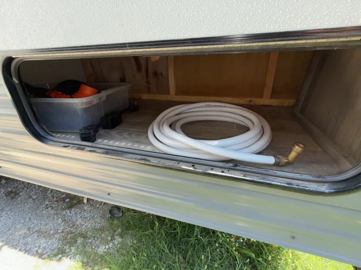 View into an RV rental storage compartment, featuring a coiled water hose, electrical adapters, and camping gear.. Gulf Stream Kingsport 2021