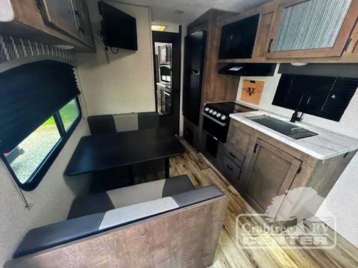 Interior of an rv rental showing a modern kitchen, booth dinette with dark table, wall-mounted TV, and bright window.. Venture Sonic 190VRB 2022