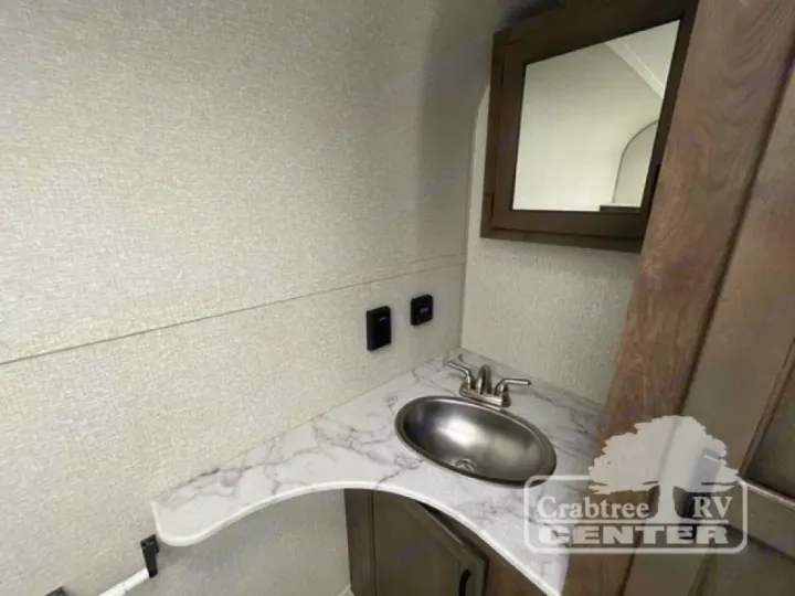 Compact RV rental bathroom vanity with an oval stainless steel sink, patterned countertop, and a wood-framed mirror.. Venture Sonic 190VRB 2022