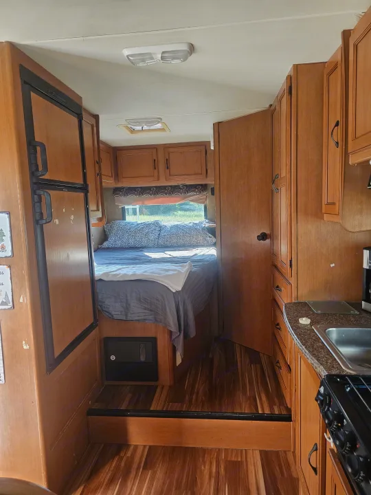 Inside a cozy RV rental: a comfortable bedroom with a window, an efficient kitchen, and fridge for your travels.. Coachmen Freelander 2014