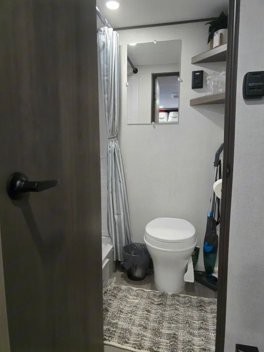 Explore a modern, compact RV rental bathroom. Features a toilet, shower, mirror, and shelves for your travel comfort.. Grand Design 151BH 2025