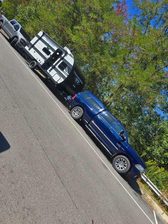 A blue pickup truck towing a Grand Design Transcend travel trailer on a sunlit road. Consider this ideal rv rental for outdoor journeys.. Grand Design 151BH 2025