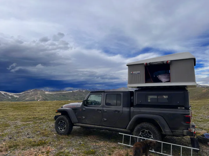 Dark grey Jeep Gladiator with a rooftop tent, an RV rental, overlooking snowy mountains under dramatic cloudy skies.. Custom Jeep Gladiator Mojave 2021