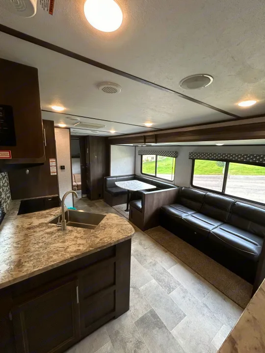 Spacious RV rental interior with a modern kitchen, U-shaped dining booth, and comfortable sofa by large windows.. Dutchmen Coleman Lantern 2020