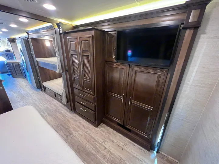 RV rental interior: bunk beds, extensive dark wood storage cabinetry with TV, and light wood-look flooring.. Entegra Coach Accolade 2022