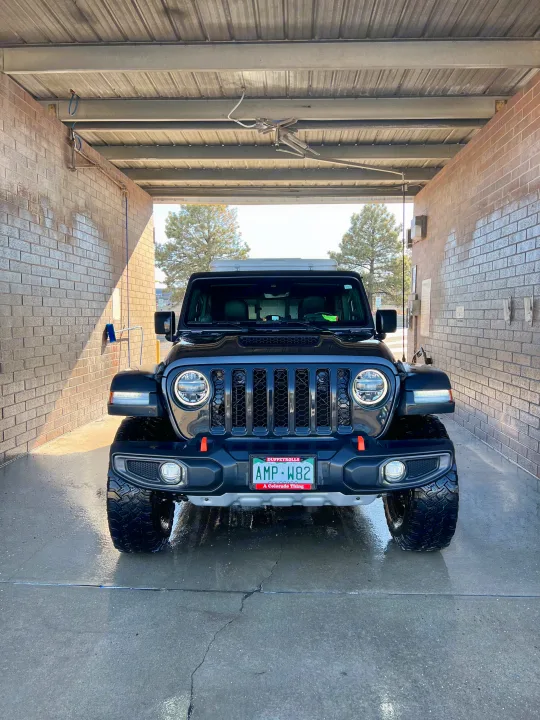 A black Jeep Gladiator with an RV rental rooftop tent, getting cleaned at a car wash, ready for Colorado adventures.. Custom Jeep Gladiator Mojave 2021