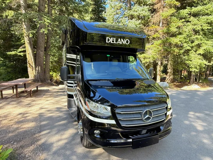Black Delano Mercedes-Benz RV rental parked in a forest setting with a picnic table nearby, ready for outdoor adventure.. Thor Delano 2022