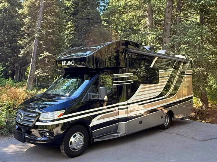 Sleek black Delano Mercedes-Benz RV rental parked among tall trees, ready for your next outdoor adventure.. Thor Delano 2022