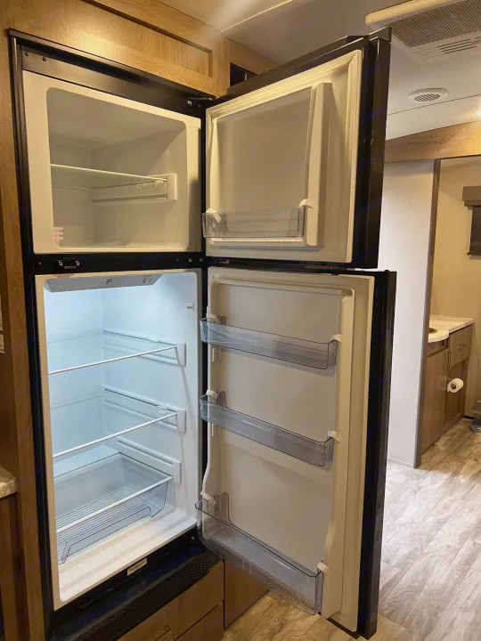 Bright, open RV rental refrigerator with separate freezer, clean shelves, and door storage, ideal for road trips.. Grand Design Imagine 2023