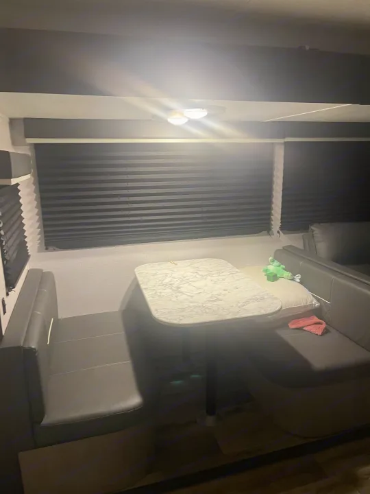 Cozy RV rental dinette featuring bench seating, a marble-look table, and closed blinds under bright overhead lights.. Dutchmen Coleman Light 2022