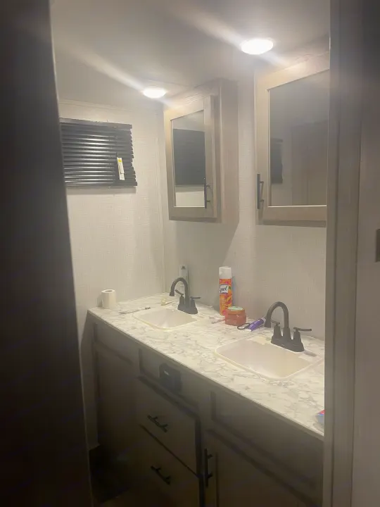 An RV rental bathroom showing a double vanity with two sinks, medicine cabinets, and bright overhead lighting.. Dutchmen Coleman Light 2022