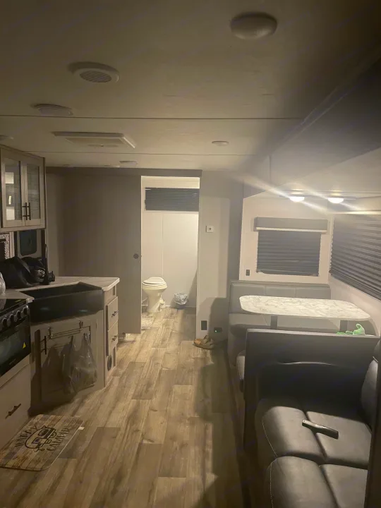 Interior of an RV rental, featuring a compact kitchen, dining booth, and living area, with the bathroom visible at the rear.. Dutchmen Coleman Light 2022