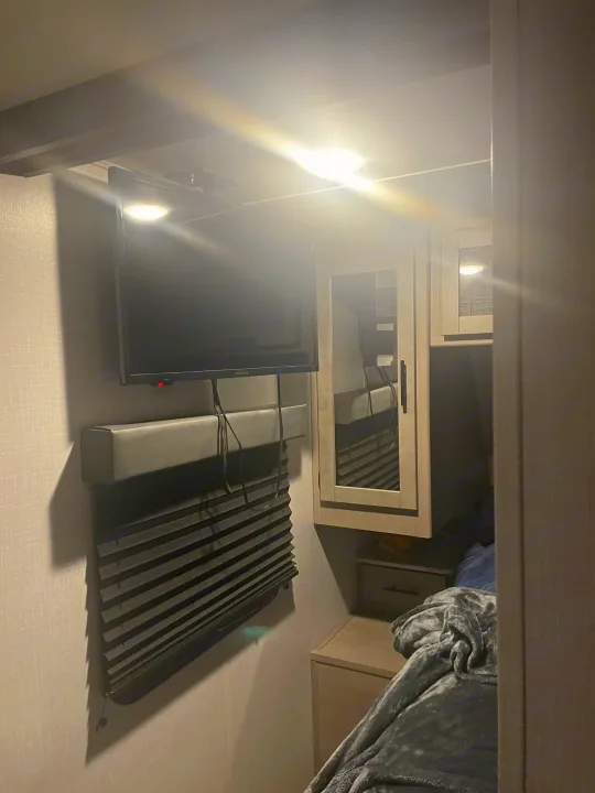 Cozy RV rental bedroom: Wall-mounted TV, closed pleated blinds, mirrored cabinet, and plush bed for a compact, comfy stay.. Dutchmen Coleman Light 2022