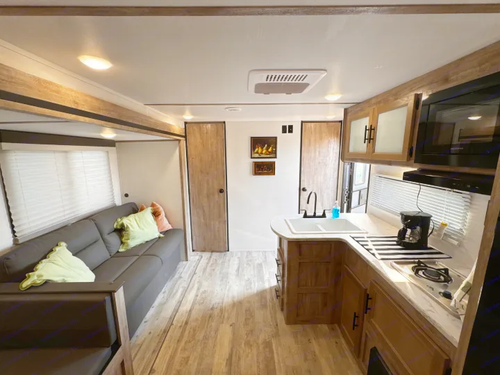 Cozy rv rental interior with a gray sofa, full kitchen (sink, stove, microwave), wood accents, and bright lighting. Ready for adventure!. Gulf Stream Enlighten 2025