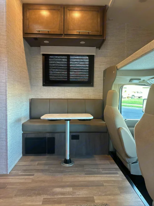 This rv rental's interior features a dining booth with a table, overhead cabinets, and a view of the front cab area. Wood-look flooring.. JAYCO REDHAWK SE 22TF 2025