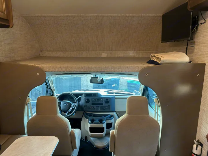 Inside an rv rental, showing the front cockpit with Ford dash, over-cab bunk bed, and a mounted TV. Ready for your road trip.. JAYCO REDHAWK SE 22TF 2025